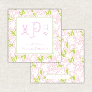 Op de afbeelding: Twee vierkante cadeaulabels met een roze bloemenpatroon en een witte rand. Het voorste label heeft de initialen "MPB" in roze, met de tekst "a gift from Morgan Pollard". Het tweede label toont het bloemenpatroon.