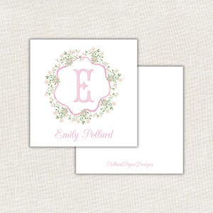 Puede incluir: Tarjeta de papelería blanca con un diseño de corona floral rosa. La letra "E" está en el centro, con el nombre "Emily Pollard" debajo. Las palabras "Pollard Paper Designs" están impresas en la segunda tarjeta.