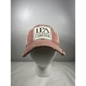 May include: A distressed maroon baseball cap featuring a rectangular white patch on the front. The patch displays the black text "IPA LOT WHEN I DRINK" in a bold, serif font. The cap has a worn, frayed edge along the brim and front panels.
