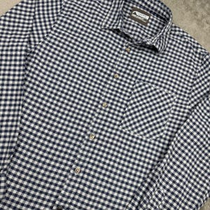 May include: A long-sleeve button-down shirt featuring a navy blue and white gingham check pattern. The shirt includes a single chest pocket, a pointed collar, and a brown interior neck label with the text Mountain Khakis Large Classic Fit.