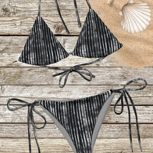 Op de afbeelding: Een tweedelige bikiniset met een zwart en grijs verticaal gestreept patroon. De top is een triangelmodel met halterbandjes en een striksluiting op de rug. Het broekje is een bikinislip met strikjes aan de zijkanten.
