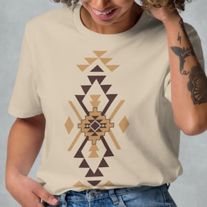 Könnte beinhalten: Beiges T-Shirt mit einem geometrischen Muster in Braun- und Beigetönen. Das Design befindet sich mittig auf der Vorderseite. Das Model trägt eine blaue Jeans. Das T-Shirt ist aus Baumwolle.