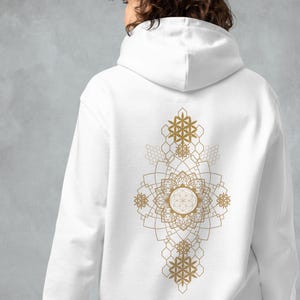 May include: White hoodie with a gold geometric mandala design on the back. The design features intricate patterns and shapes, including floral and star-like elements. The hoodie has a hood and long sleeves.