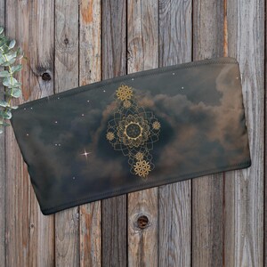 Könnte beinhalten: Ein rechteckiges, dunkel gefärbtes Stoffstück mit einem Himmelsdesign. Das Design zeigt ein zentrales, goldenes Mandala-ähnliches Muster mit strahlenförmigen Elementen und kleineren, ähnlichen Motiven. Der Hintergrund ähnelt einem bewölkten Nachthimmel mit Sternen.