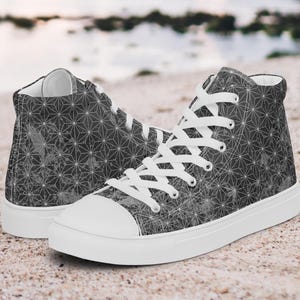 Puede incluir: Un par de zapatillas altas con un patrón geométrico en tonos grises y blancos. Los zapatos tienen cordones blancos, una puntera blanca y una suela blanca. El diseño presenta un patrón repetitivo de formas interconectadas.