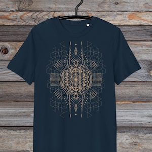 May include: Navy blue t-shirt with a geometric design in gold. The design features a central circular pattern with intersecting lines and geometric shapes. The t-shirt is hanging on a black hanger against a wooden background.