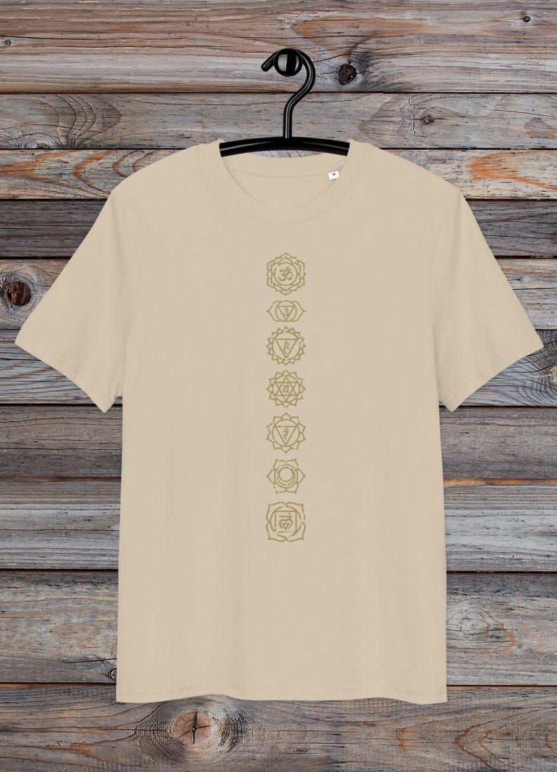 May include: A beige t-shirt with a vertical line of seven gold chakra symbols printed on the front. The symbols are in a line down the centre of the shirt.