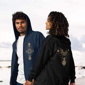 May include: Two people wearing zip-up hoodies. One is navy blue with a gold mandala design on the front. The other is black with a gold mandala design on the back. Both have hoods and front pockets.