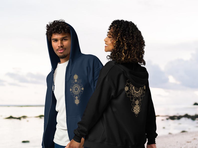 May include: Two people wearing zip-up hoodies. One is navy blue with a gold mandala design on the front. The other is black with a gold mandala design on the back. Both have hoods and front pockets.