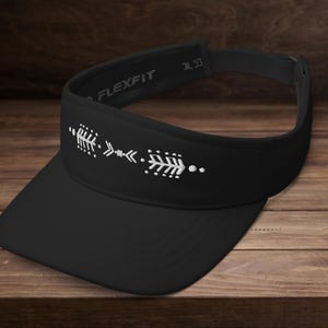 Puede incluir: Visera negra con diseño de flecha blanca. La visera tiene una visera curva y una correa ajustable. El nombre de la marca Flexfit es visible en la banda. La visera está hecha de un material ligero y está diseñada para proteger los ojos del sol.