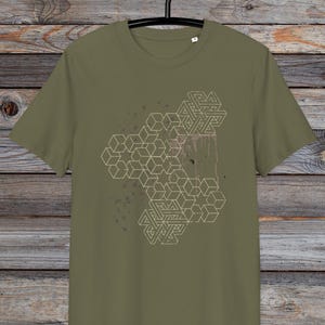 Puede incluir: Una camiseta verde con un diseño geométrico impreso en la parte delantera. El diseño presenta una serie de cubos y estrellas entrelazados en un color beige claro.