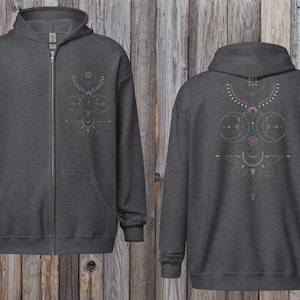 May include: Charcoal gray zip-up hoodie with a celestial design on the front and back. The design features moons, stars, and geometric shapes in a light tan color. The hoodie has a hood, a full zipper, and two front pockets.