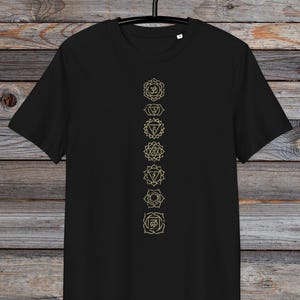 May include: Black t-shirt featuring a vertical row of seven gold chakra symbols, including the Om symbol at the top.