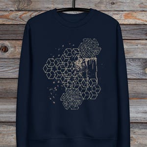 Puede incluir: Una sudadera azul marino con un diseño geométrico blanco de cubos superpuestos y un patrón de salpicaduras.