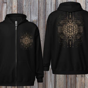 May include: Black zip-up hoodie with a gold geometric design on the front and back. The design features intricate patterns and shapes, including a central flower of life symbol. The hoodie has a hood and a full-length zipper.