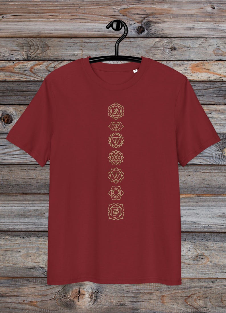 May include: A maroon t-shirt with a vertical row of seven gold chakra symbols printed on the front. The symbols are in a line down the centre of the shirt.