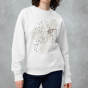 Puede incluir: Sudadera blanca con un diseño geométrico en dorado y marrón. El diseño presenta una serie de cuadrados y triángulos superpuestos, con un efecto de salpicadura en marrón.
