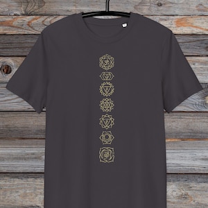 May include: A charcoal grey t-shirt with a vertical line of seven gold chakra symbols printed on the front. The symbols are in a line from top to bottom, starting with the crown chakra and ending with the root chakra.
