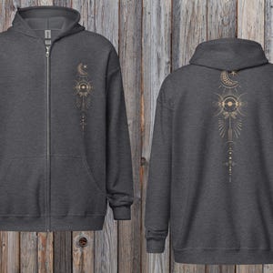 Può includere: Felpa con cappuccio e zip grigio antracite con un design celeste dorato. La parte anteriore presenta un piccolo disegno sul petto, mentre il retro mostra un'illustrazione dettagliata di luna, sole e stelle. La felpa ha cappuccio e tasche anteriori.