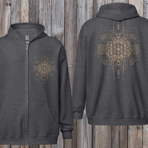 Puede incluir: Sudadera con capucha gris oscuro con cremallera y un detallado diseño geométrico dorado en la parte delantera y trasera. El diseño presenta patrones y formas intrincados. La sudadera tiene capucha y bolsillos delanteros.