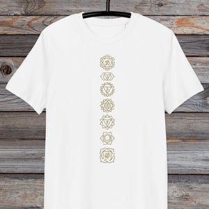 May include: White t-shirt with a vertical line of seven gold chakra symbols printed on the front.