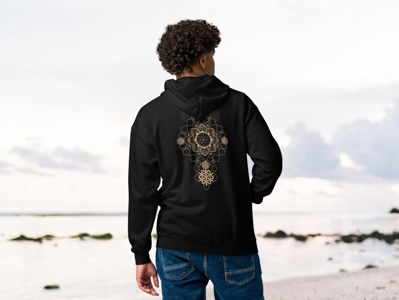 May include: Black hoodie with a gold geometric design on the back. The design features a central circular element with radiating patterns and a series of interconnected shapes. The hoodie has a hood and long sleeves.