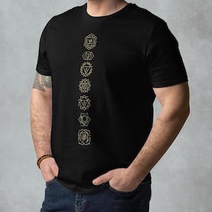 May include: A black t-shirt with a vertical line of seven gold chakra symbols printed on the front. The symbols are in a line from top to bottom, starting with the crown chakra and ending with the root chakra.