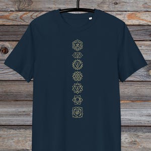 May include: A navy blue t-shirt with a vertical row of seven gold chakra symbols printed on the front. The symbols are in a line down the centre of the shirt.