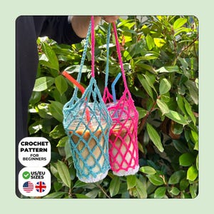 May include: Two crochet cup holders with long handles, one in light blue and one in bright pink, each featuring a diamond-shaped mesh pattern and a white base. The holders contain clear plastic cups filled with iced coffee and colorful straws.