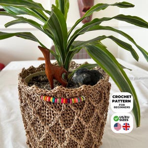 May include: A woven crochet plant pot with a colorful beaded accent. The pot holds a green plant with long leaves and a wooden animal figurine. The image includes text that says "CROCHET PATTERN FOR BEGINNERS" and "US/EU SIZES".