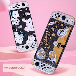 May include: Two Switch OLED cases with unique designs. One features white cats on a black background, the other has astronaut cats, rockets, and the word "Rocket" on a black and yellow background. The cases are white and black.