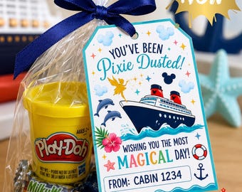 May include: A clear plastic gift bag tied with a navy blue ribbon containing a yellow Play-Doh container and miniature candy bars. A tag attached reads: You've been Pixie Dusted! Wishing you the most magical day! From: Cabin 1234, featuring a cruise ship.