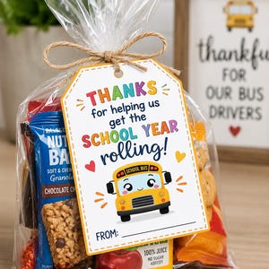 May include: A clear plastic gift bag filled with assorted snacks, including a granola bar and juice box, tied with twine. A white rectangular tag features a yellow school bus illustration and the text: THANKS for helping us get the SCHOOL YEAR rolling!