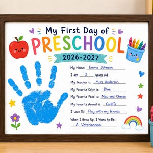 May include: A framed My First Day of Preschool 2026-2027 sign with a blue handprint, a red apple, and a blue crayon cup illustration. The text includes fields for name, age, teacher, favorite color, food, animal, hobbies, and future career goals.