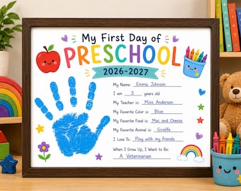 Op de afbeelding: Een ingelijst My First Day of Preschool 2026-2027 bord met een blauwe handafdruk, een rode appel en een blauwe beker met kleurpotloden. De tekst bevat velden voor naam, leeftijd, leraar, favoriete kleur, eten, dier, hobby's en toekomstplannen.