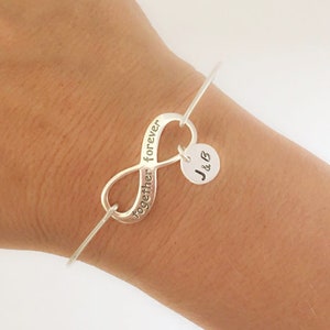 May include: Silver infinity charm bracelet with the words "together forever" engraved on the charm. The bracelet also features a small round charm with the initials "J & B" engraved on it.