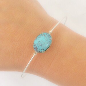 May include: A silver bangle bracelet with a turquoise oval-shaped stone set in the centre.