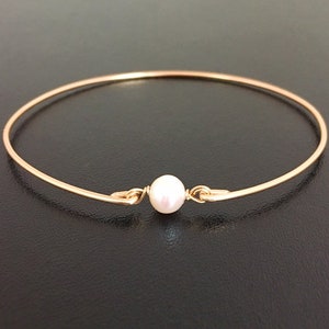May include: A delicate gold bangle bracelet with a single white pearl accent. The bracelet is simple and elegant, perfect for everyday wear.