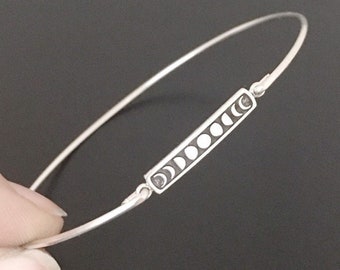 May include: A silver bangle bracelet with a rectangular charm featuring a moon phase design.