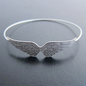 May include: A silver bangle bracelet with a detailed wing design. The wings are intricately patterned and have a delicate, feminine feel.