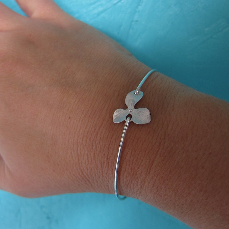 Op de afbeelding: Een zilveren armband met een delicate bloembedel. De bedel is getextureerd en heeft een kleine cirkel in het midden.