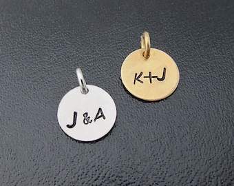 May include: Two round metal charms with initials engraved on them. The charm on the left is silver and says "J&A". The charm on the right is gold and says "K+J".