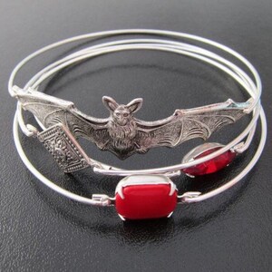 Pu&ograve; includere: Tre braccialetti in argento con un ciondolo a forma di pipistrello in argento e due ciondoli di pietre preziose rosse.