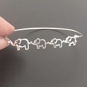 Puede incluir: Una pulsera de plata con una cadena delicada y cuatro encantos de elefante recortados. Los elefantes est&aacute;n mirando en la misma direcci&oacute;n y est&aacute;n conectados por sus trompas.