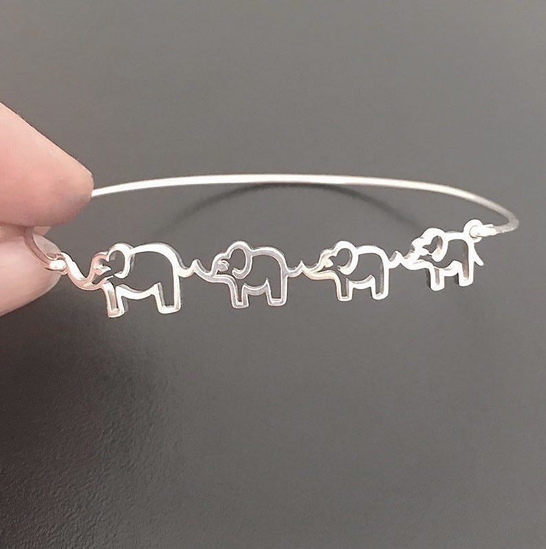 Puede incluir: Una pulsera de plata con una cadena delicada y cuatro encantos de elefante recortados. Los elefantes est&aacute;n mirando en la misma direcci&oacute;n y est&aacute;n conectados por sus trompas.