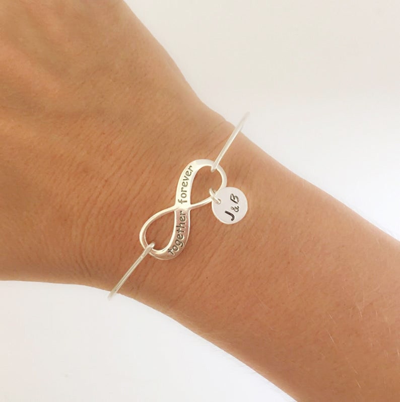 May include: Silver infinity charm bracelet with the words "together forever" engraved on the charm. The bracelet also features a small round charm with the initials "J & B" engraved on it.