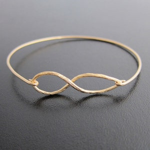 May include: A gold infinity symbol bangle bracelet. The bracelet is made of thin wire and has a hammered finish.