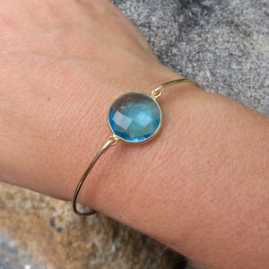 May include: A gold bangle bracelet with a large, round, light blue gemstone.