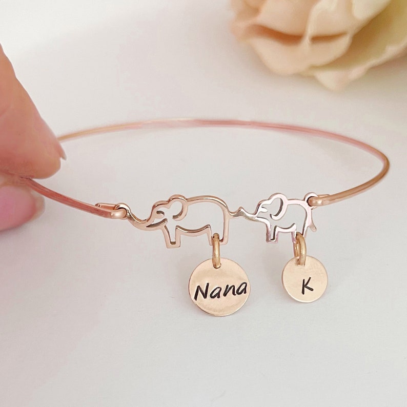 May include: Rose gold bangle bracelet with two elephant charms and two round charms. One charm says "Nana" and the other charm says "K".