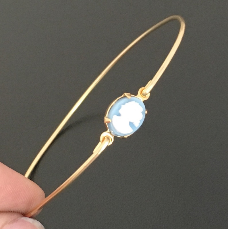 May include: A gold bangle bracelet with a light blue cameo featuring a white silhouette of a woman's profile.